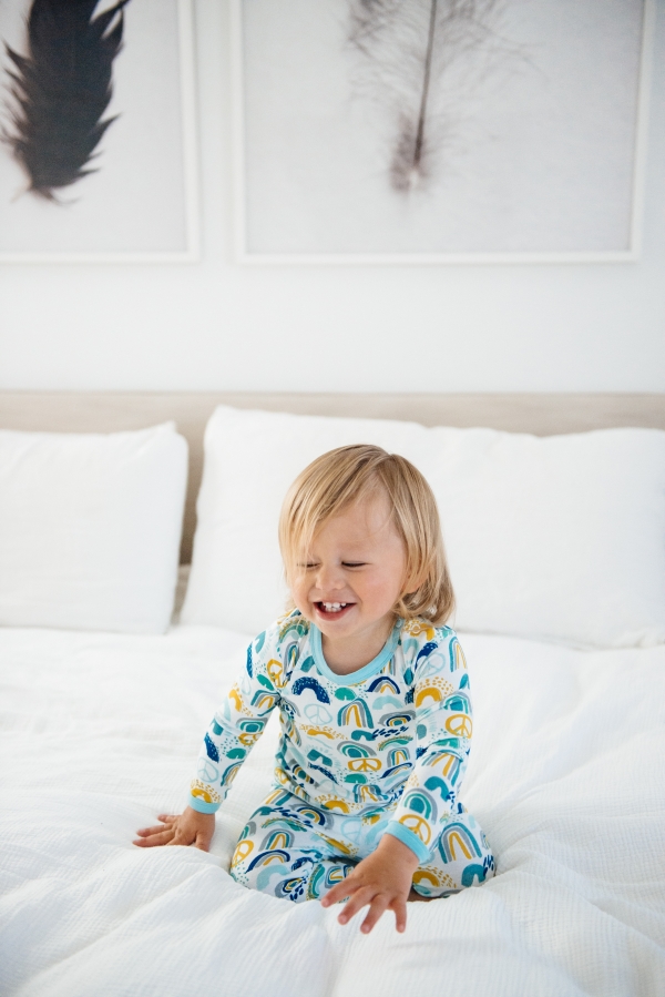 Toddler laughing on bed in Clover Baby & Kids pajamas celebrating Rainbow Baby, IVF, and Infertility