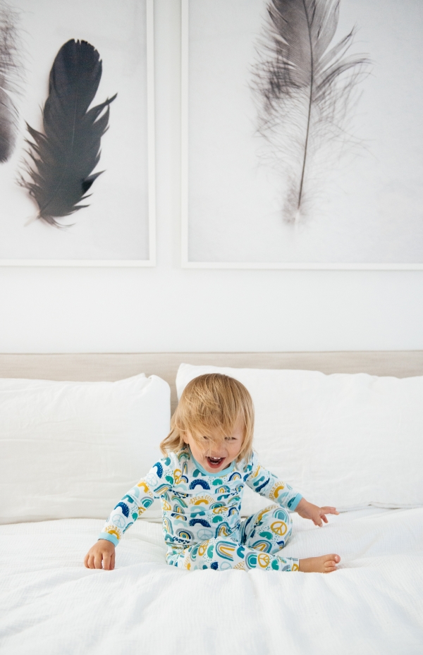 Toddler laughing on bed in Clover Baby & Kids pajamas celebrating Rainbow Baby, IVF, and Infertility