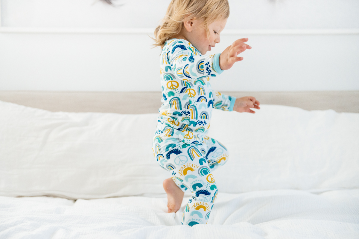 Toddler jumping on bed in Clover Baby & Kids pajamas celebrating Rainbow Baby, IVF, and Infertility