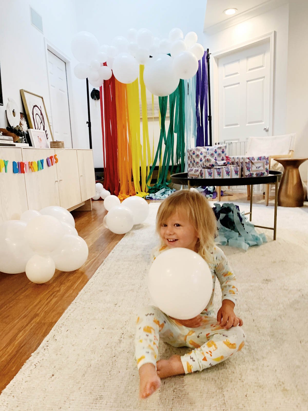 Otis holding balloons and DIY Rainbow and cloud balloon arch with streamer backdrop for Trolls Themed Birthday