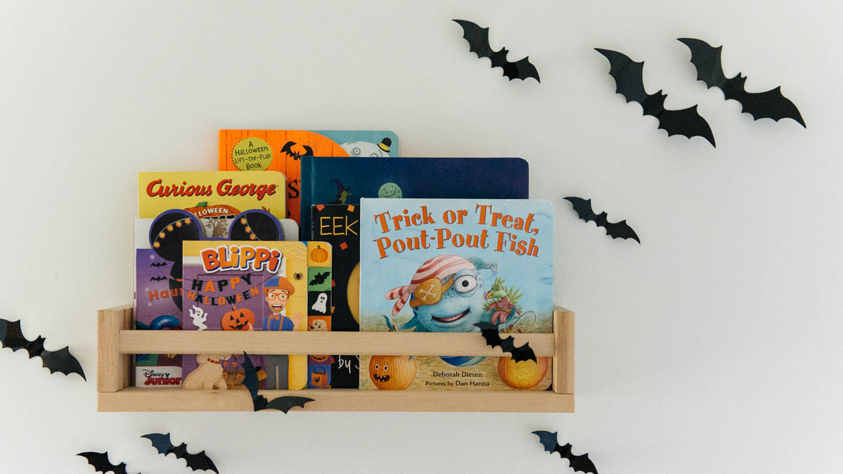 Best Halloween Books for Toddlers styled on wooden shelves with bat wall decals 
