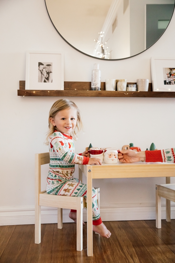 Indoor Holiday decor of toddler sitting at kids table with Santa Clause mugs in Christmas pajamas