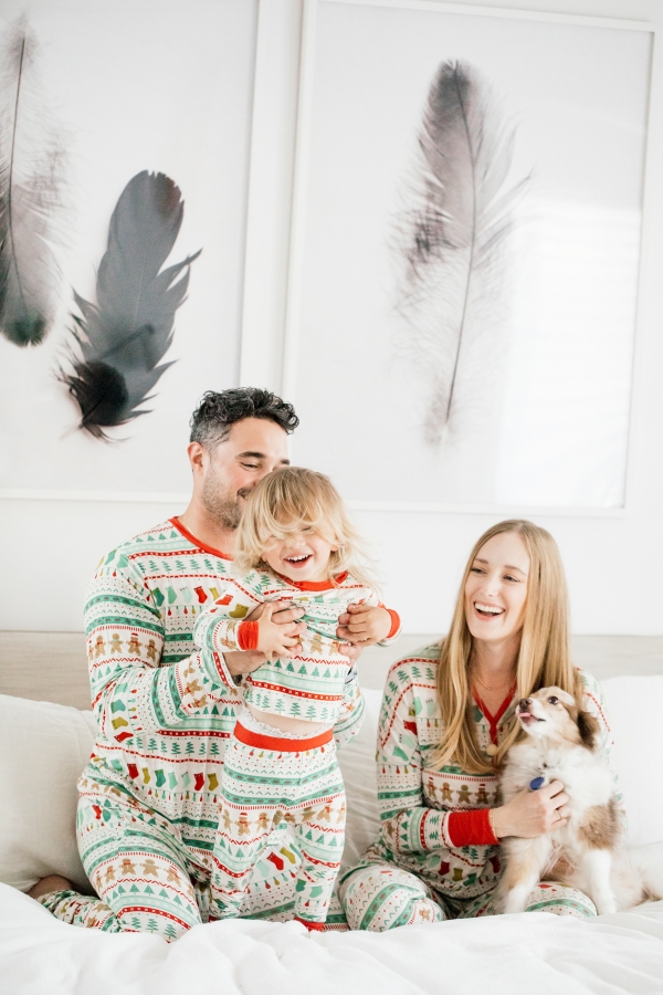 Family in matching Holiday pajamas laughing on the bed
