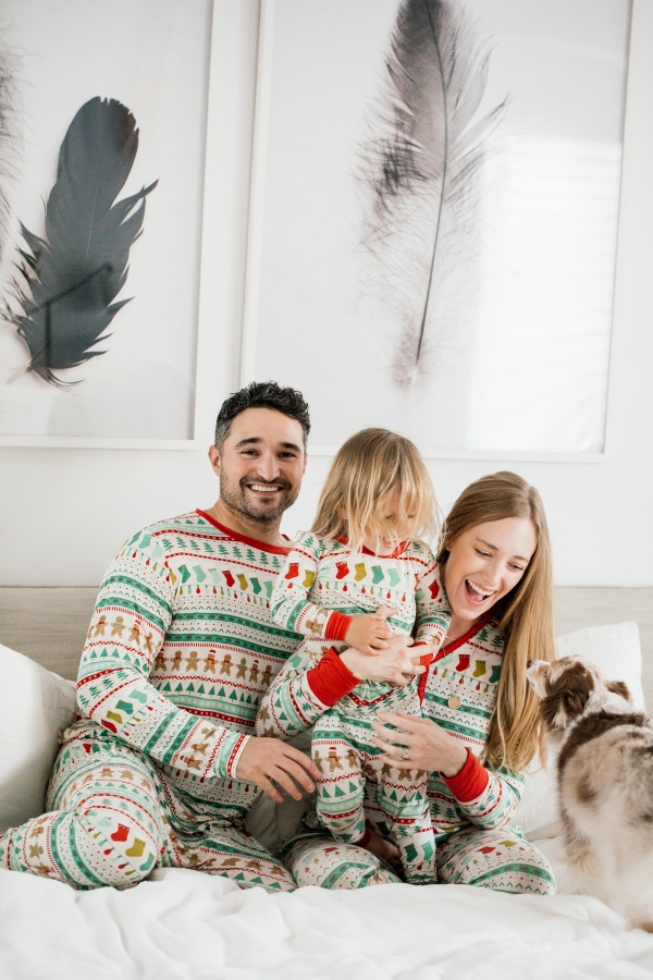 Family in matching Holiday pajamas laughing on the bed
