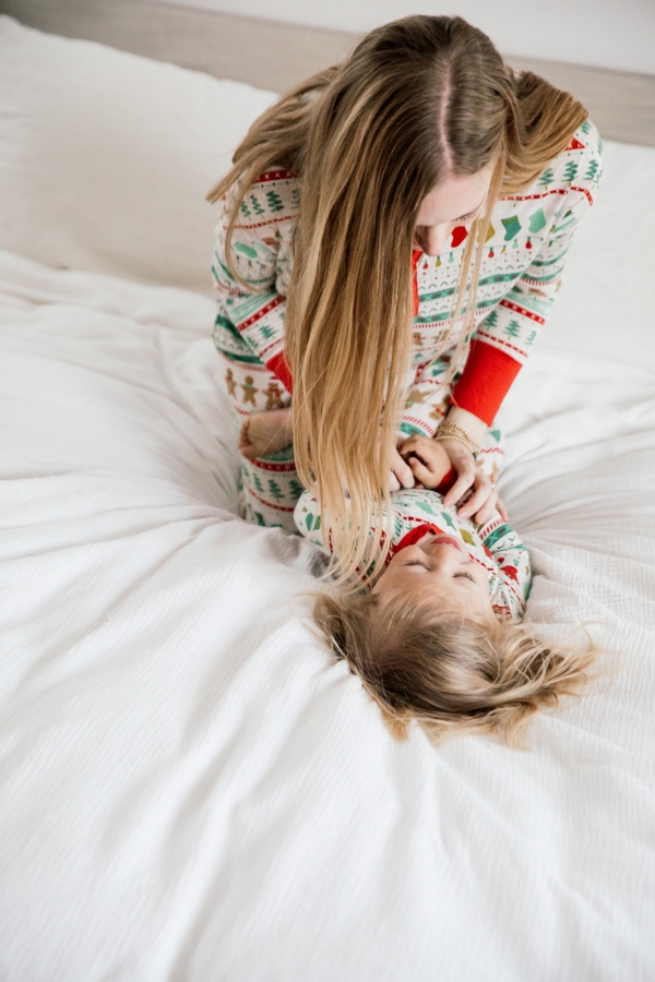 Mother and son in matching Holiday pajamas laughing on the bed
